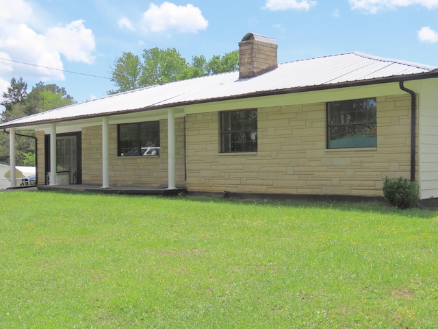 back of property with a lawn, stone siding, a chimney, and metal roof