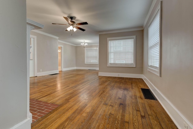 empty room featuring wood finished floors, a chandelier, ceiling fan, crown molding, and healthy amount of natural light
