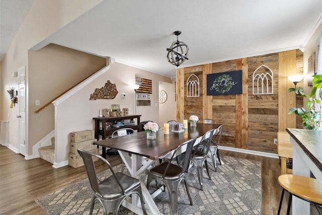 dining area with stairs, dark wood-style flooring, wooden walls, ornamental molding, and a chandelier