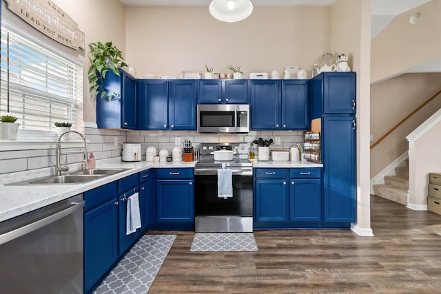 kitchen with appliances with stainless steel finishes, a sink, blue cabinetry, and backsplash