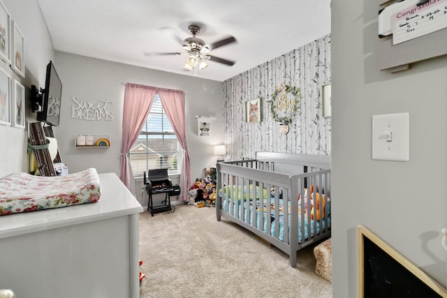 bedroom featuring a nursery area, carpet flooring, a ceiling fan, and wallpapered walls