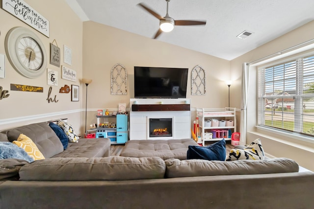 living area with vaulted ceiling, ceiling fan, and a warm lit fireplace