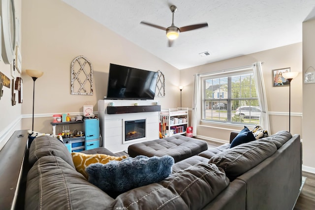 living room featuring lofted ceiling, dark wood-style flooring, baseboards, ceiling fan, and a glass covered fireplace