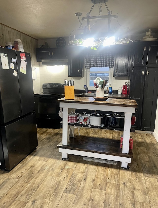 kitchen featuring black appliances, wood-type flooring, dark cabinets, and under cabinet range hood