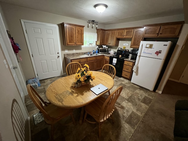 kitchen featuring brown cabinetry, a sink, freestanding refrigerator, stainless steel microwave, and black range with electric cooktop
