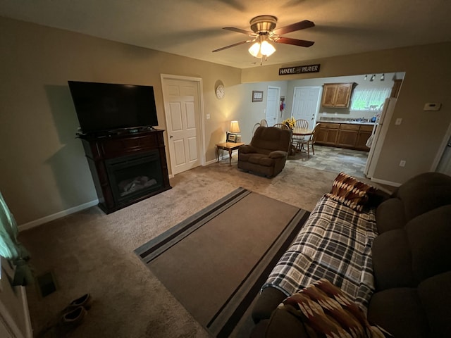 carpeted living room with baseboards, a fireplace, and a ceiling fan