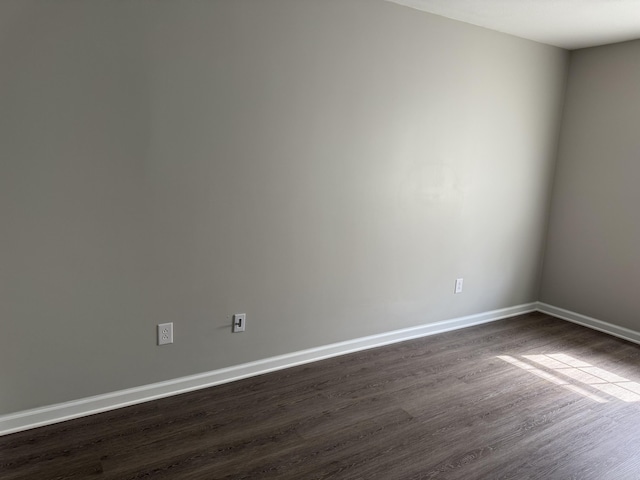 spare room featuring baseboards and dark wood-type flooring