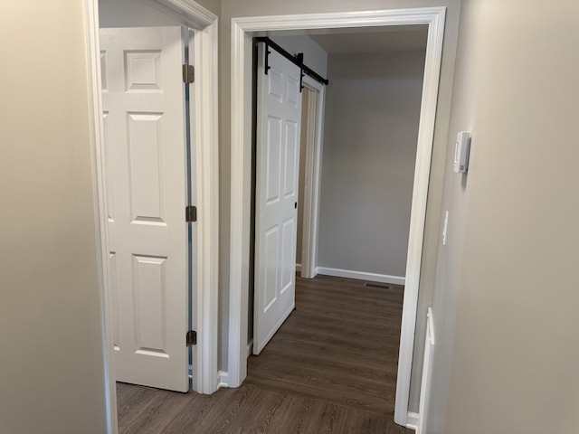 hall featuring baseboards, dark wood-style flooring, a barn door, and visible vents