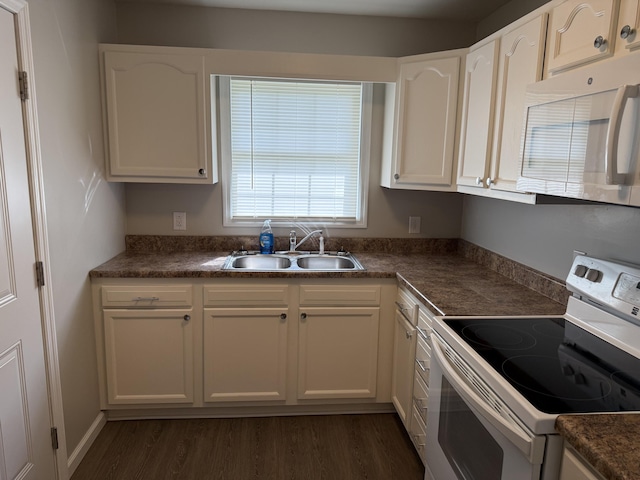 kitchen with white cabinets, dark countertops, a sink, white appliances, and dark wood finished floors