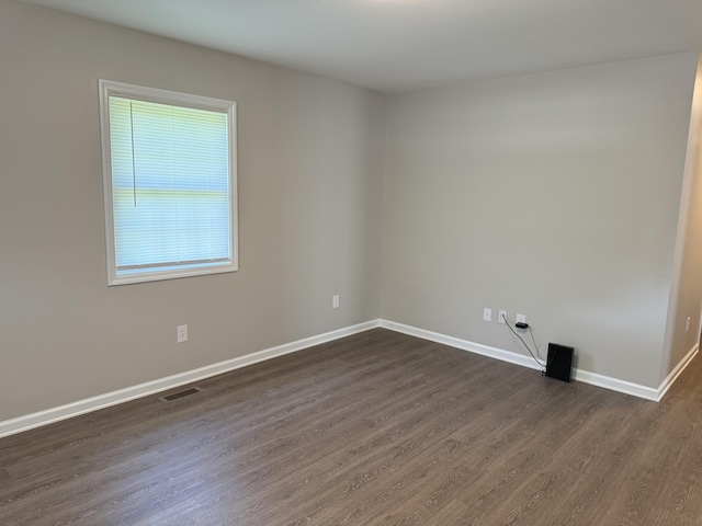 unfurnished room with baseboards, dark wood-style floors, and visible vents