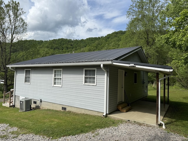 view of side of property with metal roof, a lawn, a carport, a view of trees, and entry steps