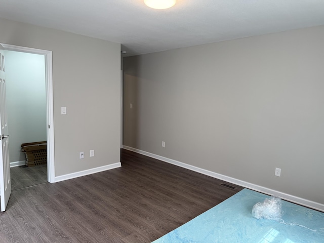unfurnished room featuring baseboards, visible vents, and dark wood-type flooring