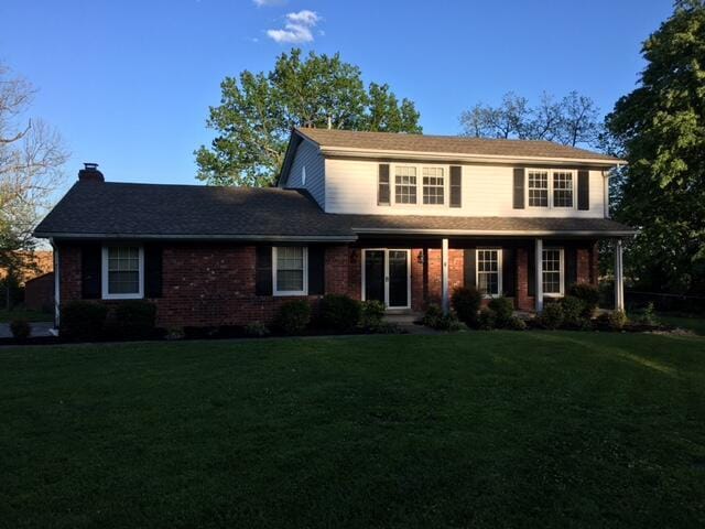 traditional-style house with brick siding, a chimney, and a front lawn