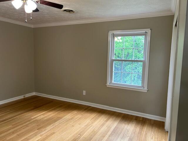 spare room featuring crown molding, light wood-style floors, a textured ceiling, a ceiling fan, and baseboards
