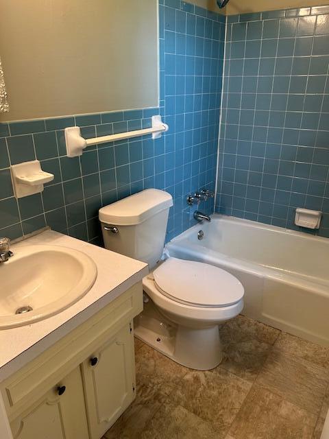 bathroom featuring tile walls, bathtub / shower combination, vanity, a wainscoted wall, and toilet