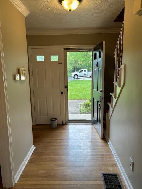 entrance foyer featuring a textured ceiling, light wood-style flooring, baseboards, ornamental molding, and stairway