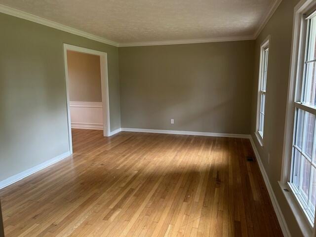 unfurnished room featuring wood-type flooring, baseboards, ornamental molding, and a healthy amount of sunlight