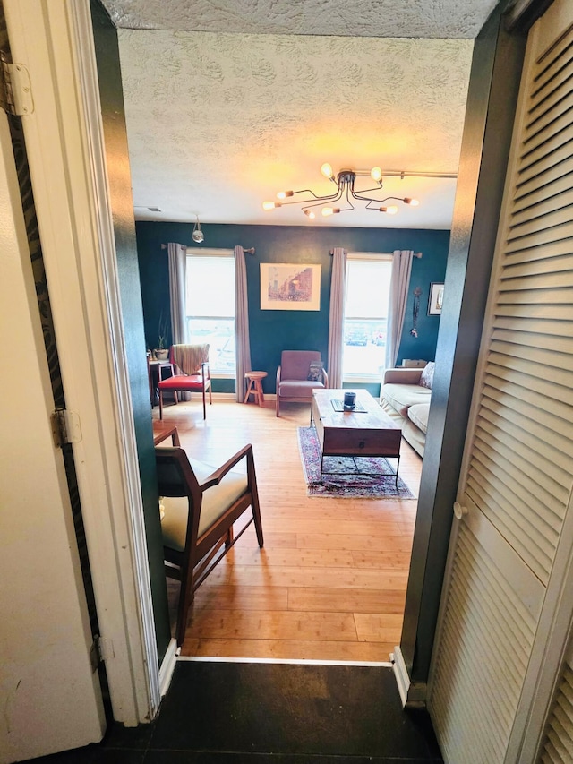 corridor featuring wood-type flooring, a textured ceiling, a notable chandelier, and plenty of natural light