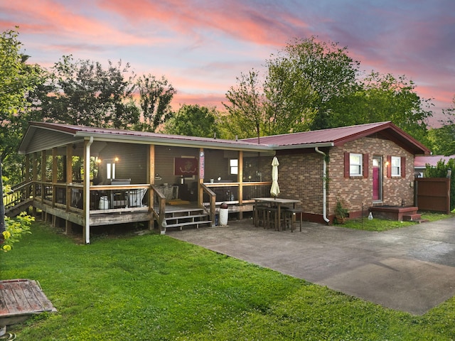 88 Plum St, Stanton, KY 40380 - back of house at dusk featuring a yard, metal roof, a wooden deck, a patio, and brick siding