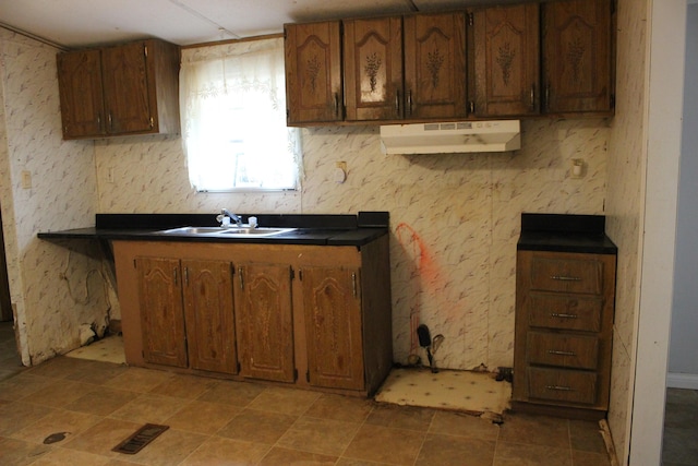 kitchen featuring under cabinet range hood, a sink, dark countertops, and brown cabinets