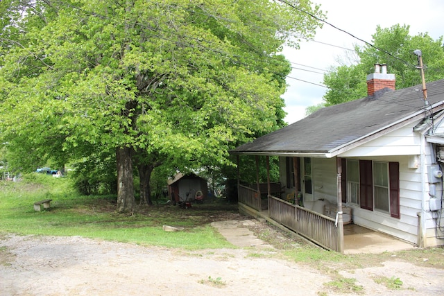 view of home's exterior with a storage shed, a chimney, an outdoor structure, a porch, and roof with shingles