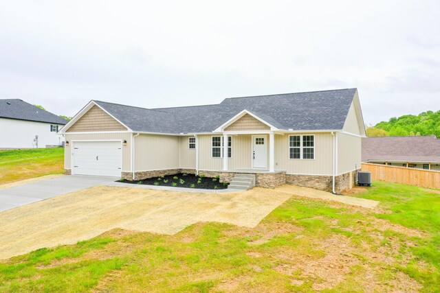 single story home featuring driveway, an attached garage, roof with shingles, central AC unit, and covered porch