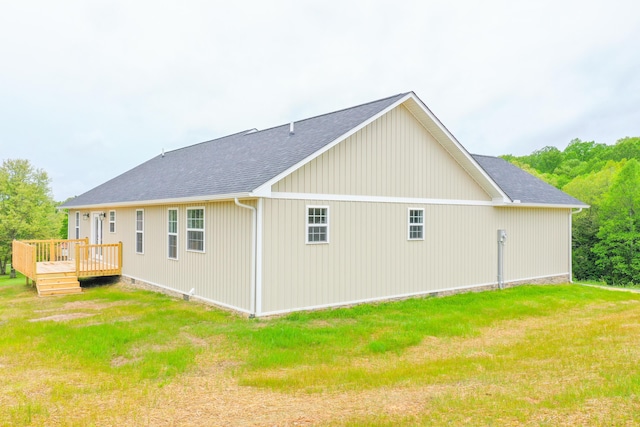 view of side of property with a deck, a shingled roof, and a lawn