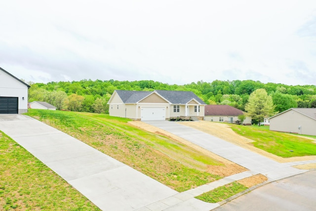 view of front of property featuring driveway, a front lawn, a forest view, and an attached garage