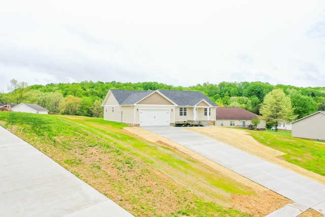 single story home with driveway, an attached garage, a front yard, and a view of trees