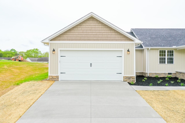 view of front facade featuring a garage, driveway, a front yard, stone siding, and a shingled roof