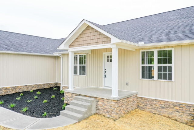 entrance to property featuring stone siding, a porch, and roof with shingles