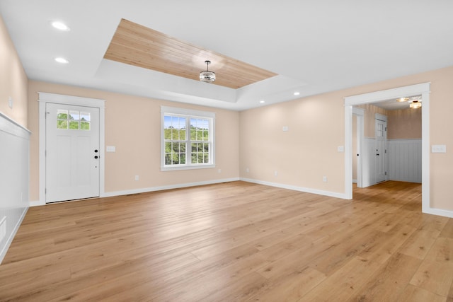 unfurnished living room featuring a raised ceiling, light wood-style flooring, plenty of natural light, baseboards, and recessed lighting