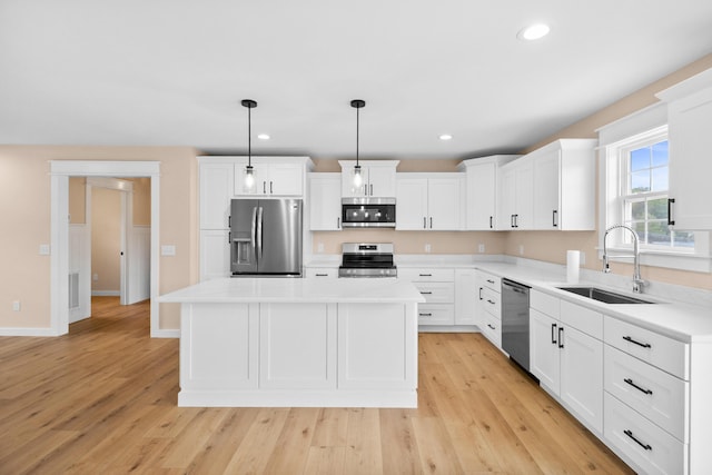 kitchen featuring stainless steel appliances, a sink, a center island, light countertops, and light wood-style flooring