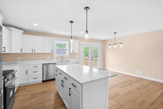 kitchen with stainless steel appliances, a sink, light wood-type flooring, a center island, and white cabinets