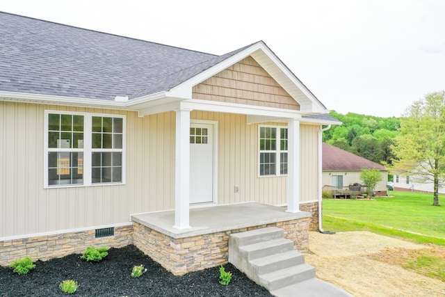 doorway to property featuring roof with shingles, a yard, and a porch