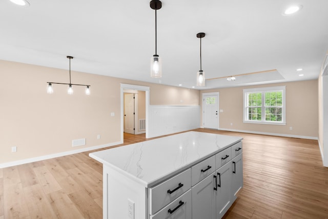 kitchen featuring open floor plan, light wood finished floors, hanging light fixtures, light stone counters, and a kitchen island