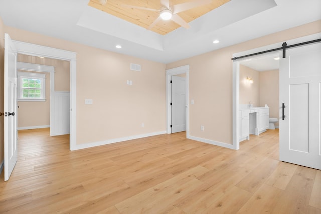 unfurnished bedroom featuring a barn door, a raised ceiling, light wood-style flooring, wooden ceiling, and baseboards