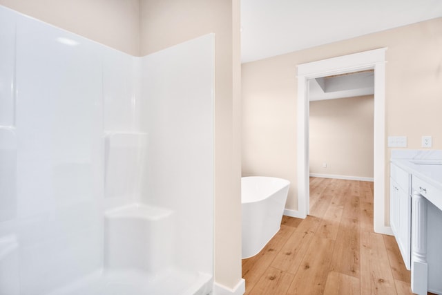 bathroom featuring hardwood / wood-style flooring, a freestanding bath, a shower, vanity, and baseboards