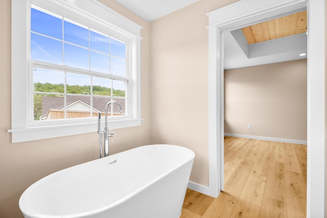 bathroom featuring wood finished floors, baseboards, a freestanding tub, and wood ceiling