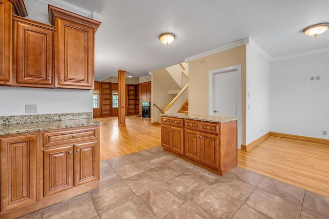 kitchen featuring light wood finished floors, brown cabinetry, crown molding, and light stone counters