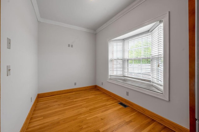 empty room with light wood-type flooring, visible vents, baseboards, and ornamental molding