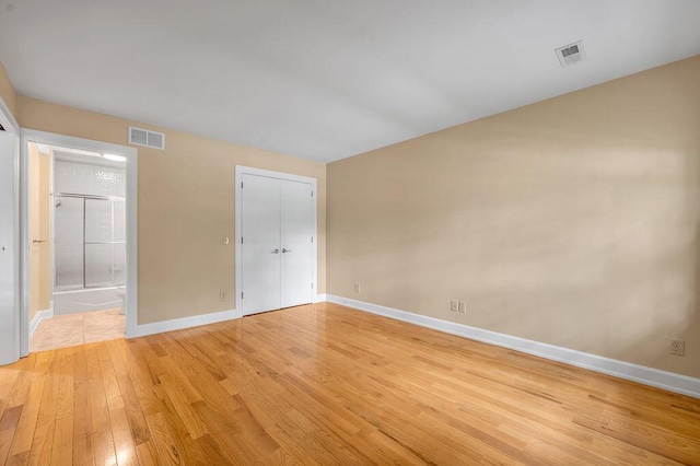 unfurnished bedroom with baseboards, ensuite bath, light wood finished floors, and visible vents