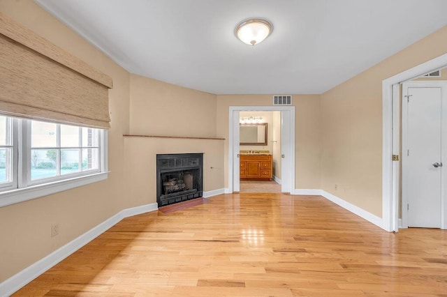 unfurnished living room with baseboards, light wood-style floors, a fireplace, and visible vents