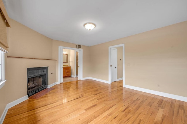 unfurnished living room with baseboards, visible vents, light wood-style flooring, and a fireplace with flush hearth