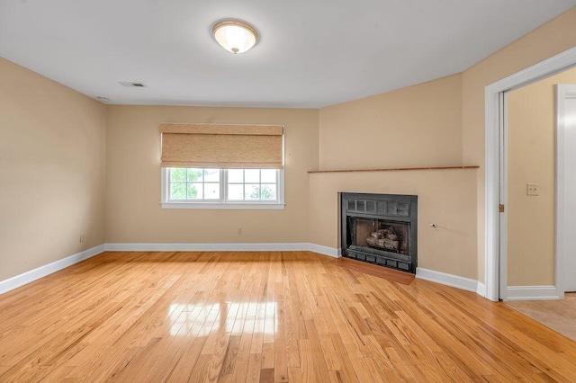 unfurnished living room featuring baseboards, a fireplace, visible vents, and wood finished floors