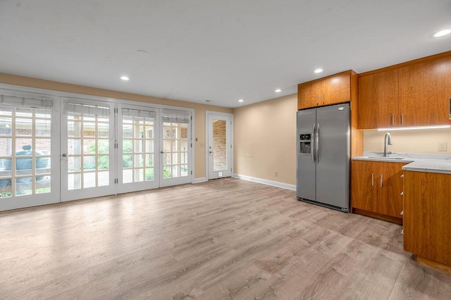 kitchen featuring a sink, brown cabinets, stainless steel refrigerator with ice dispenser, light wood finished floors, and light countertops