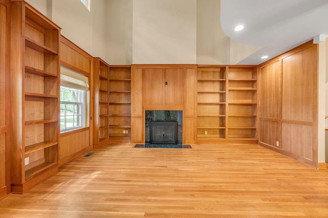 unfurnished living room with light wood-style floors, a high end fireplace, visible vents, and a towering ceiling