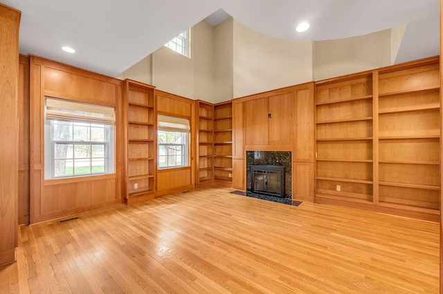 unfurnished living room with a high end fireplace, a towering ceiling, visible vents, built in shelves, and light wood-style floors