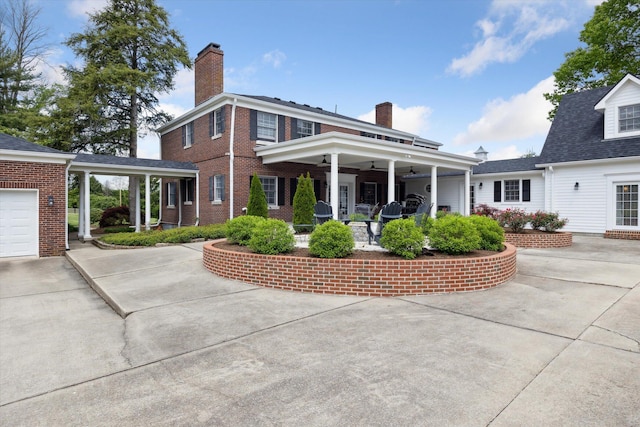 view of front facade with a ceiling fan, a chimney, brick siding, and driveway