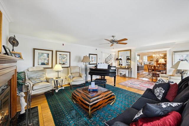 living area with wood-type flooring, ceiling fan, ornamental molding, and a fireplace
